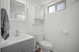 Bathroom with toilet, vanity, wood finished floors, and baseboards