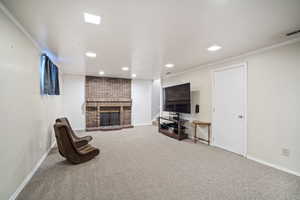 Carpeted living room featuring a brick fireplace, ornamental molding, baseboards, and recessed lighting