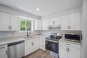 Kitchen with stainless steel appliances, a sink, under cabinet range hood, white cabinets, and recessed lighting