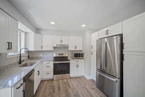 Kitchen featuring appliances with stainless steel finishes, a sink, under cabinet range hood, light wood-style flooring, and white cabinets