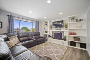 Living area with wood finished floors, ornamental molding, recessed lighting, a fireplace with raised hearth, and built in features