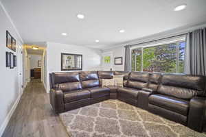 Living area with wood finished floors, recessed lighting, ornamental molding, and baseboards