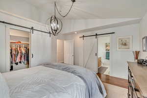 Bedroom with a barn door, lofted ceiling, dark wood-type flooring, a walk in closet, and baseboards