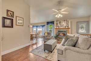 Living room with baseboards, wood-type flooring, a ceiling fan, and a fireplace