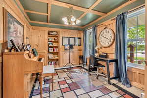 Office area featuring coffered ceiling, a chandelier, wooden walls, plenty of natural light, and crown molding