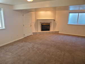 Unfurnished basement living room featuring a tiled fireplace, carpet, and baseboards