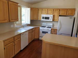 Kitchen featuring white appliances, a sink, dark wood-style floors, light countertops, and lofted ceiling