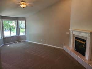 Unfurnished living room featuring dark colored carpet, a fireplace, vaulted ceiling, and a ceiling fan