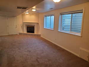 Unfurnished basement living room with carpet floors, a fireplace, baseboards, and a textured ceiling