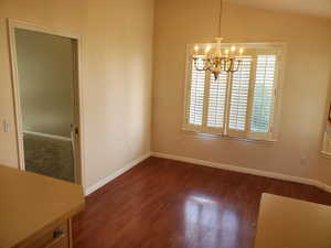 Unfurnished dining area featuring dark wood-type flooring, a chandelier, and lofted ceiling