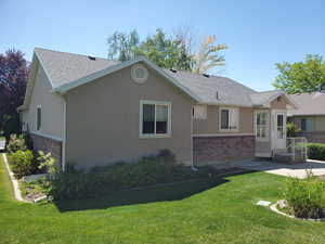 View of front of house with brick siding, a shingled roof, stucco siding, a front lawn, and a patio