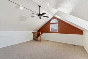 Bonus room or bedroom with a ceiling fan, wainscoting, lofted ceiling, carpet flooring, and a textured ceiling
