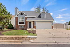 Tri-level home with driveway, brick siding, a garage, roof with shingles, and a chimney