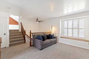Carpeted living room with ceiling fan and stairs
