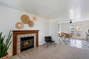 Living area with a ceiling fan, a textured ceiling, a tiled fireplace, and tile patterned floors