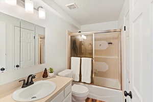 Bathroom with vanity, toilet, a textured ceiling, and shower / bath combination with glass door