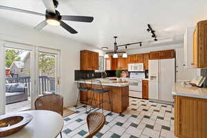 Kitchen with white appliances, a peninsula, a sink, light countertops, and ceiling fan