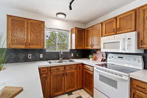 Kitchen with white appliances, a sink, light countertops, and brown cabinetry