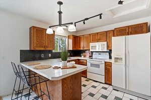 Kitchen featuring white appliances, a peninsula, light countertops, and brown cabinetry