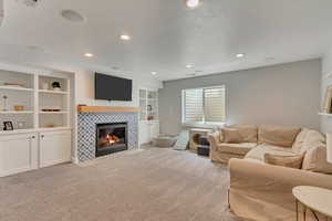 Carpeted living area featuring a tiled fireplace, built in features, and recessed lighting
