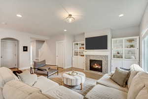 Living area with light wood finished floors, a fireplace, stairway, arched walkways, and recessed lighting