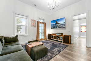 Living area with baseboards, an inviting chandelier, visible vents, crown molding, and wood finished floors