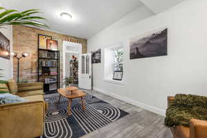 Living room featuring a textured ceiling, wood finished floors, baseboards, and brick wall