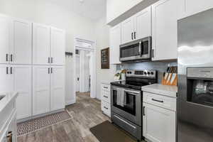 Kitchen with baseboards, decorative backsplash, light wood-style floors, white cabinets, and appliances with stainless steel finishes