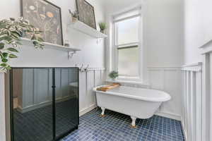 Bathroom featuring tile patterned floors, a decorative wall, a freestanding tub, and a wainscoted wall