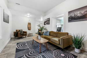 Living room with light wood-type flooring, baseboards, visible vents, and a textured ceiling