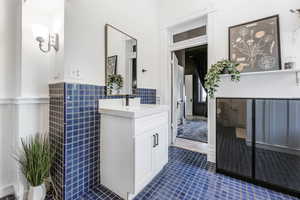 Bathroom with tile walls, tile patterned floors, vanity, and a wainscoted wall