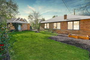 Rear view of property with a yard, a shingled roof, a chimney, and brick siding