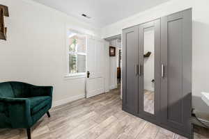Living area with crown molding, light wood-type flooring, visible vents, and baseboards