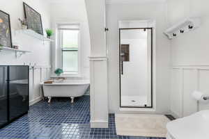 Bathroom with a decorative wall, a stall shower, tile patterned flooring, wainscoting, and a freestanding bath