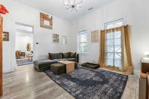 Living area featuring wood finished floors, a notable chandelier, crown molding, visible vents, and baseboards