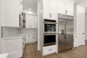 Kitchen with stainless steel appliances, light wood finished floors, white cabinetry, backsplash, and light countertops