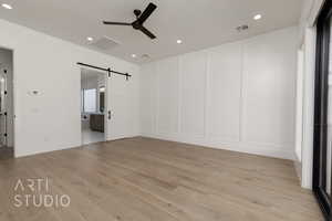 Unfurnished bedroom with a barn door, a decorative wall, recessed lighting, light wood-style floors, and connected bathroom