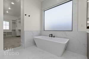 Full bathroom featuring marble finish flooring, tile walls, a freestanding tub, and recessed lighting