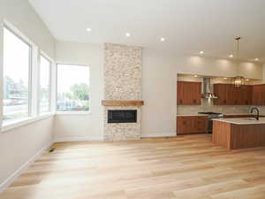Kitchen featuring stainless steel range, wall chimney range hood, open floor plan, light countertops, and a fireplace