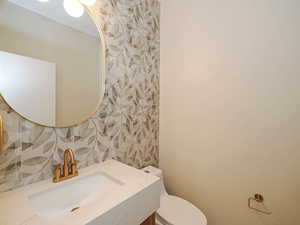 Bathroom featuring toilet, wallpapered walls, and vanity