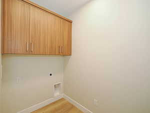 Washroom with hookup for an electric dryer, cabinet space, baseboards, and light wood-type flooring