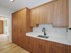 Kitchen featuring a sink, light wood finished floors, light stone counters, and brown cabinetry