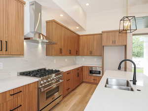 Kitchen featuring stainless steel stove, wall chimney range hood, a sink, backsplash, and recessed lighting