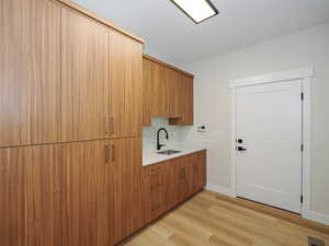 Laundry area featuring a sink, light wood-style flooring, and baseboards