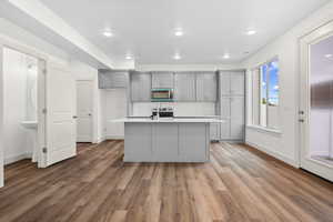 Kitchen with gray cabinetry, light countertops, light wood finished floors, stainless steel microwave, and a center island with sink
