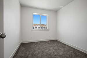 Spare room featuring dark colored carpet and baseboards