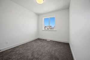 Spare room featuring dark carpet and baseboards