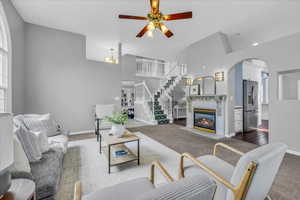 Living room with ceiling fan, carpet floors, arched walkways, baseboards, and a towering ceiling