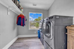 Clothes washing area with washing machine and dryer, wood finished floors, and baseboards