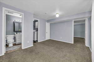 Unfurnished bedroom featuring carpet floors, washer / dryer, a spacious closet, baseboards, and ensuite bath